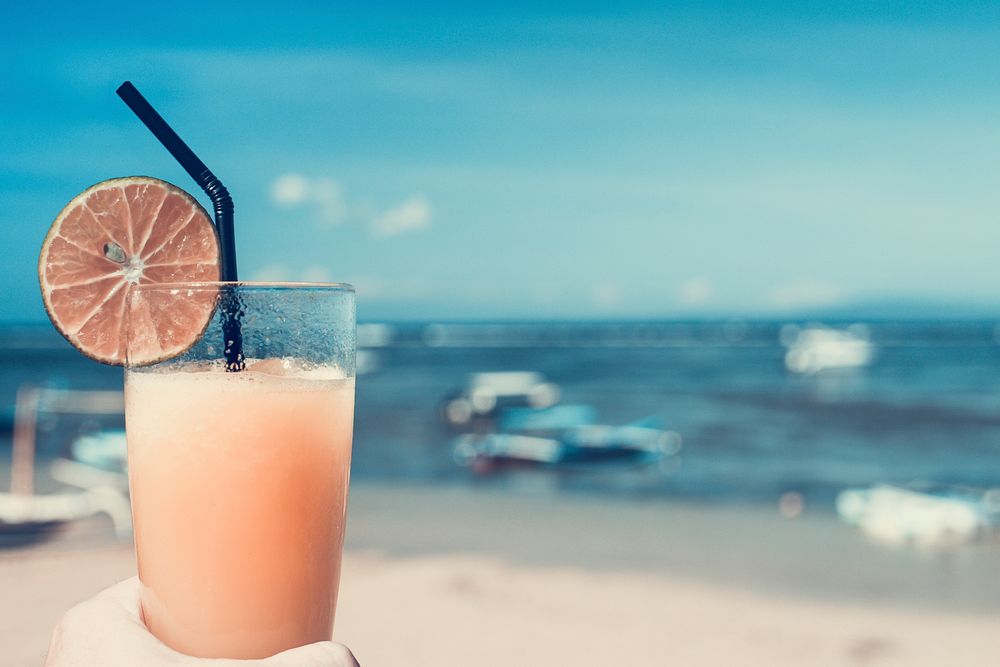 A glass of fresh and cold orange juice against the background of the sea. Free public domain CC0 photo.