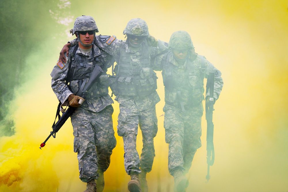 U.S. Army Pfc. Tim Hofmann, left, and Spc. Alex Sidoa, right, help Army Sgt. Michael Barnes through smoke marking a…