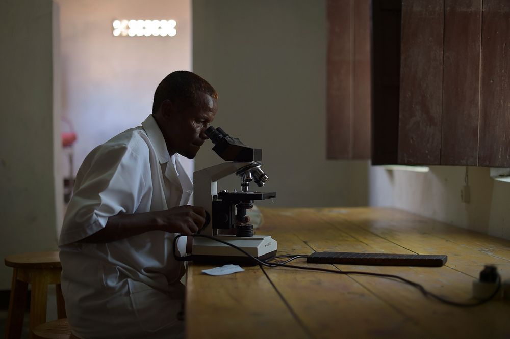 A lab technician checks a blood sample for malaria in Barawe, Somalia, on August 23, 2016. Original public domain image from…