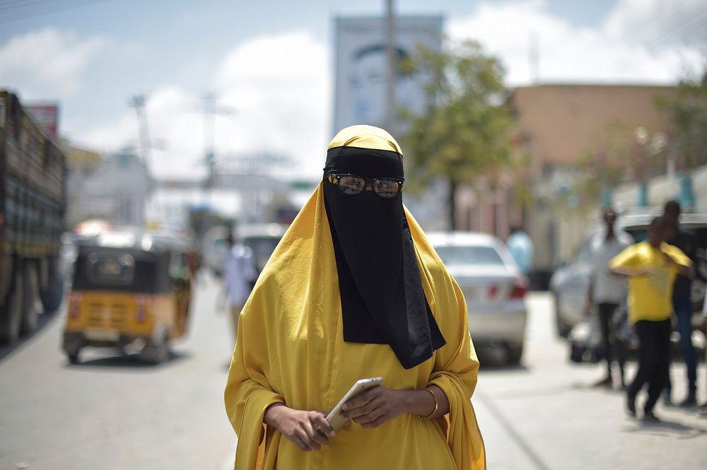 A Somali student stands on the sidewalk of a road in downtown Mogadishu in front of a billboard advertising one of the…