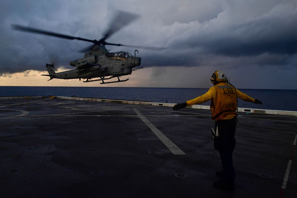 U.S. Navy Aviation Boatswain’s Mate (Handling) Airman Anthony Similton, from Augusta, Georgia, directs a Marine Corps AH-1Z…