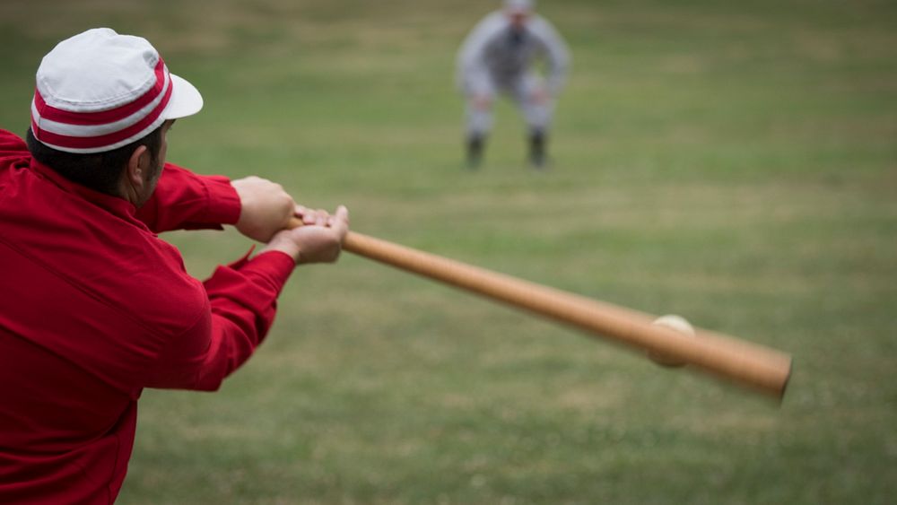 A batter swings at a ball during a historic baseball game being played where uniforms of the period are worn and they follow…
