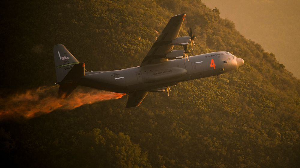 A U.S. Air National Guard C-130J equipped with the MAFFS 2 (Modular Airborne Fire Fighting System) drops a line of Phos-Chek…
