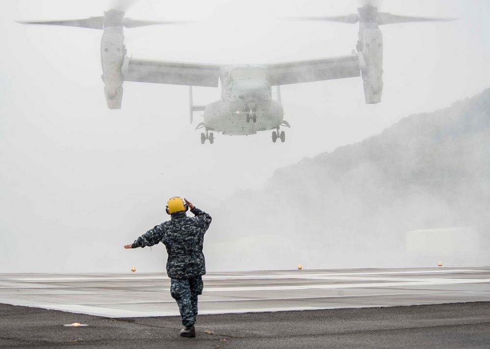 U.S. Navy Boatswain's Mate 1st Class Carlglo Rula directs an MV-22 Osprey tiltrotor aircraft attached to Marine Medium…