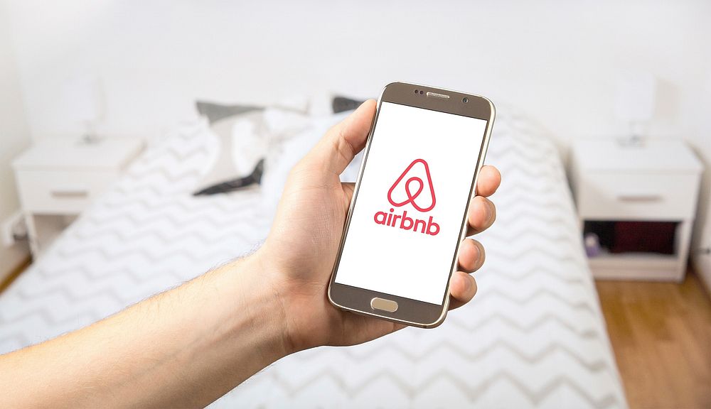 Hand posing with a smartphone showing Airbnb logo on it's screen, location unknown, date unknown.