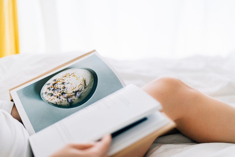 Free woman reading recipe book in bed photo, public domain CC0 image.