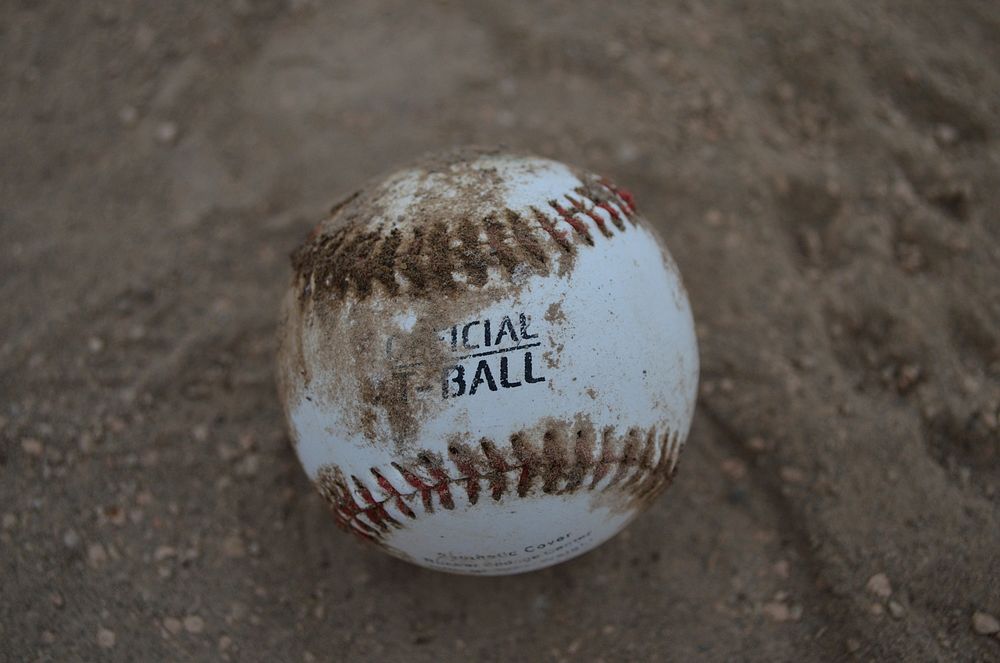 Closeup on baseball in sand. Free public domain CC0 photo.