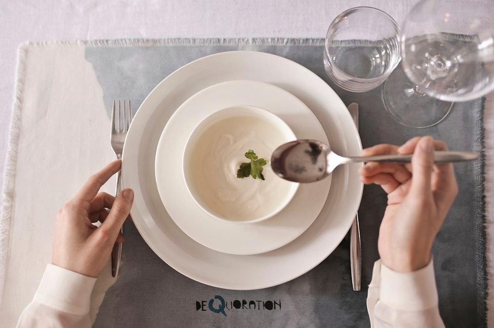 A closeup of soup bowl plate and cutlery with female hands