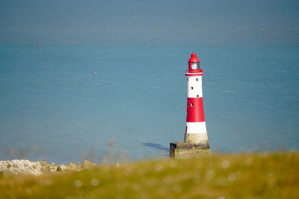 Red and white lighthouse on cliff by seashore. Free public domain CC0 photo.