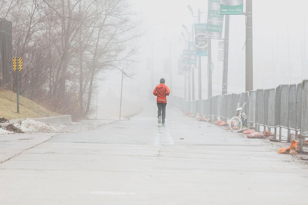 Back view of a person wearing orange color jacket jogging on a foggy day