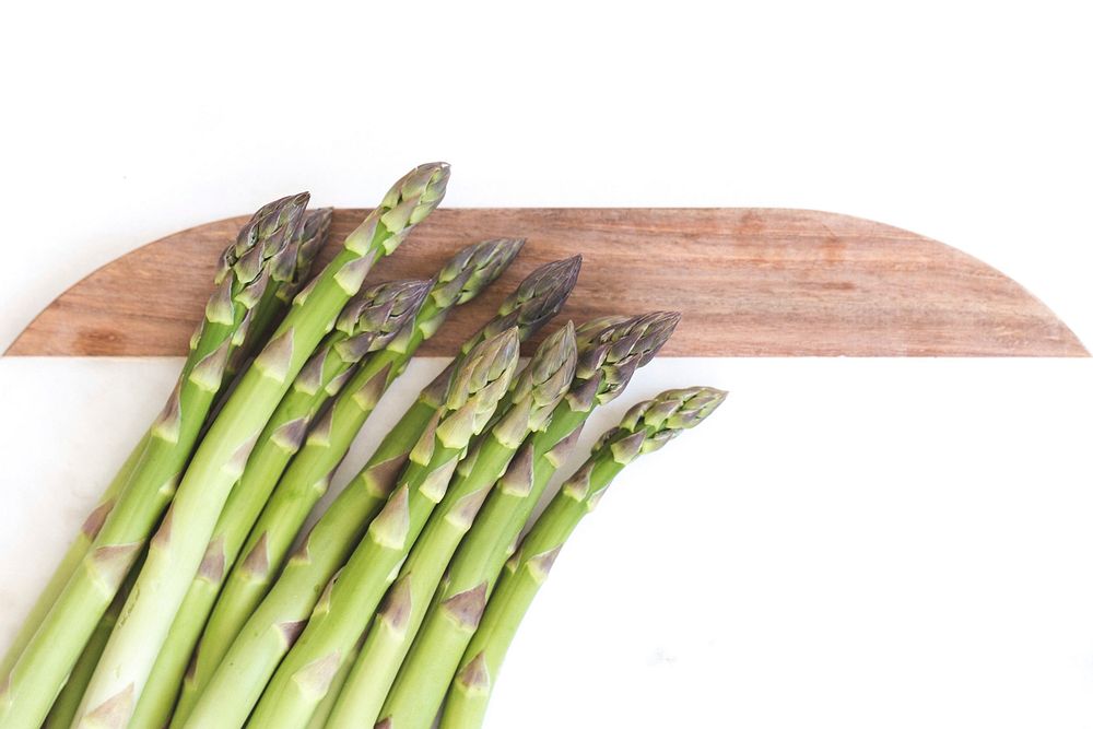A pile of fresh asparagus on cutting board white background