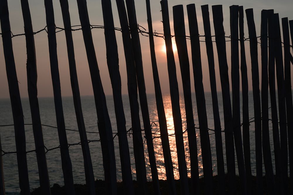 Beach sunset through wooden fence. Free public domain CC0 photo.