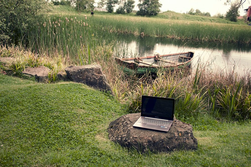 Free laptop on rock with rowboat in a lake image, public domain CC0 photo.