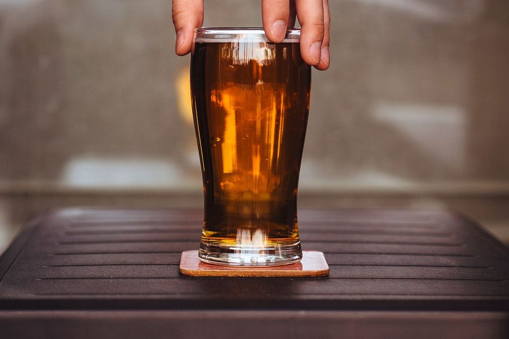 Free hand holding beer glass on wooden table photo, public domain beverage CC0 image.