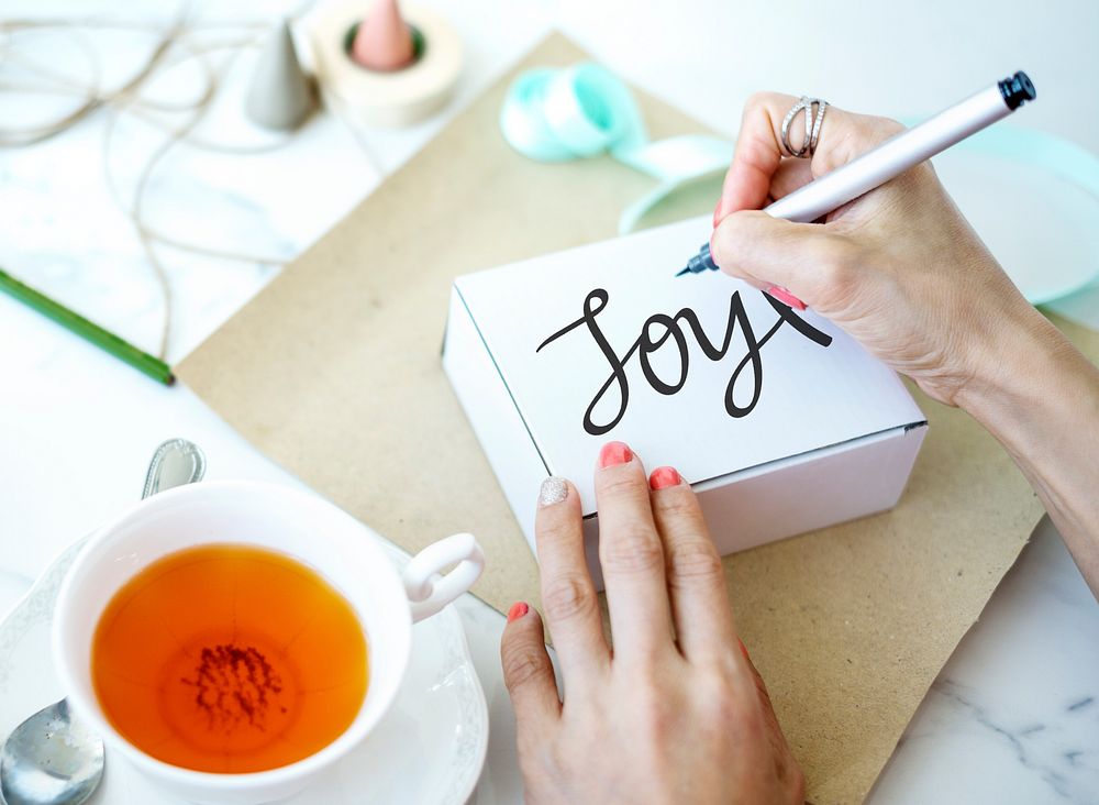 Woman writing a word Joy on a gift box