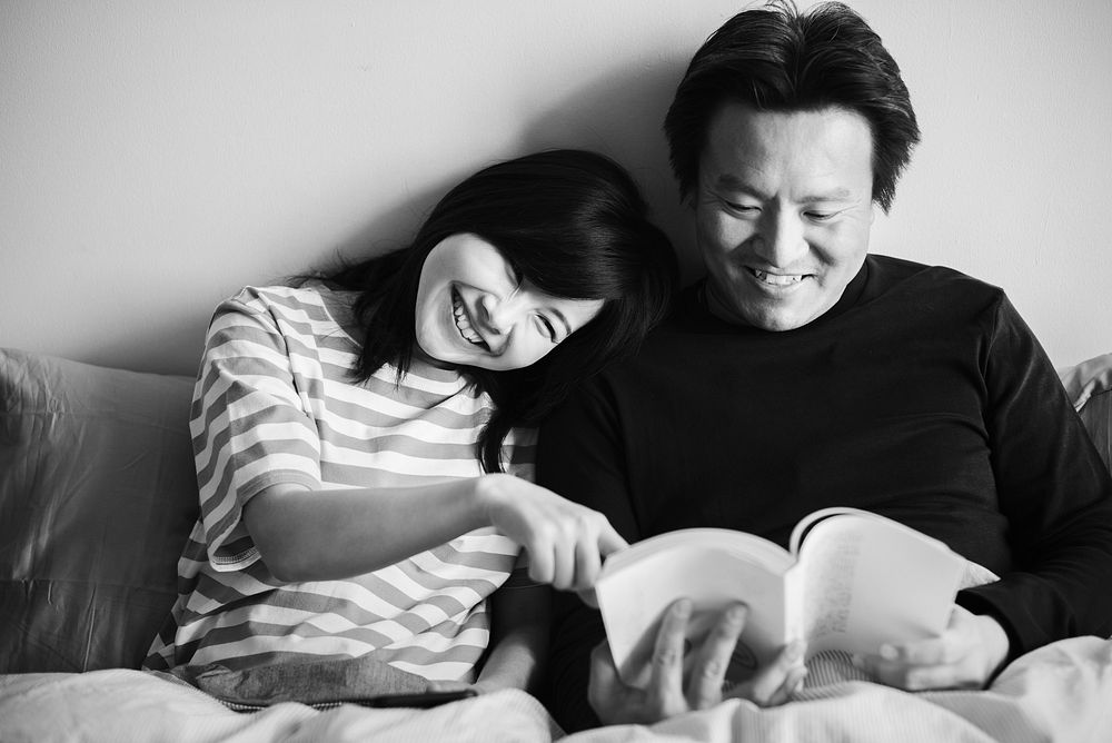 Asian couple reading a book in bed together