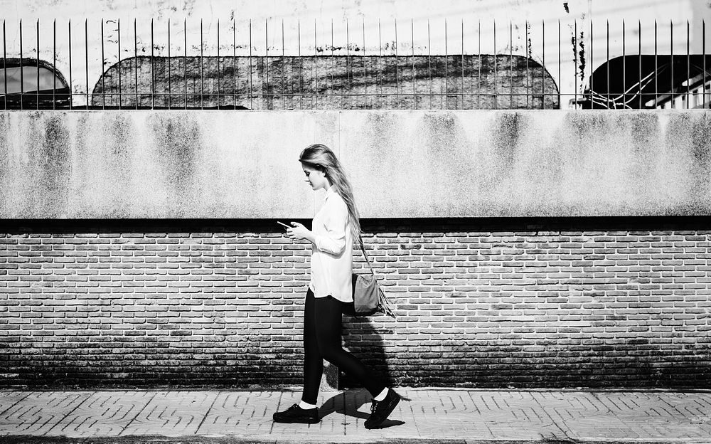 Young woman using smartphone and walking