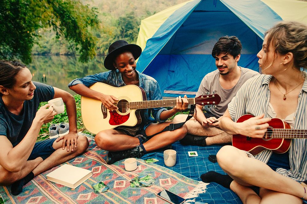 Group of young adult friends at a campsite playing guitar