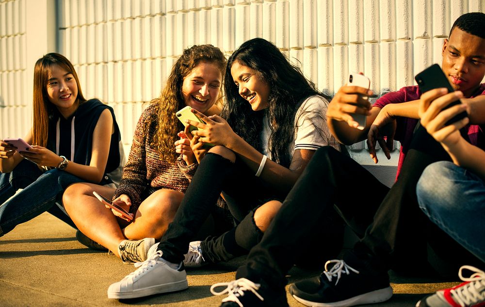 Young teenage friends chilling out together and using smartphones