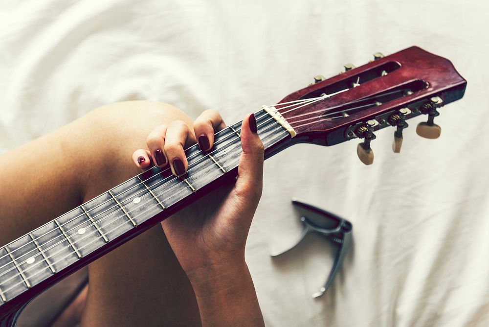 Woman playing guitar on her bed