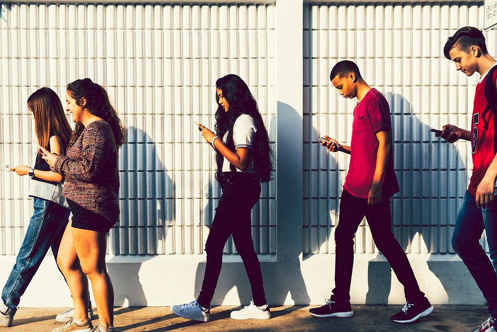 Group of young teenager friends walking home after school using smartphones