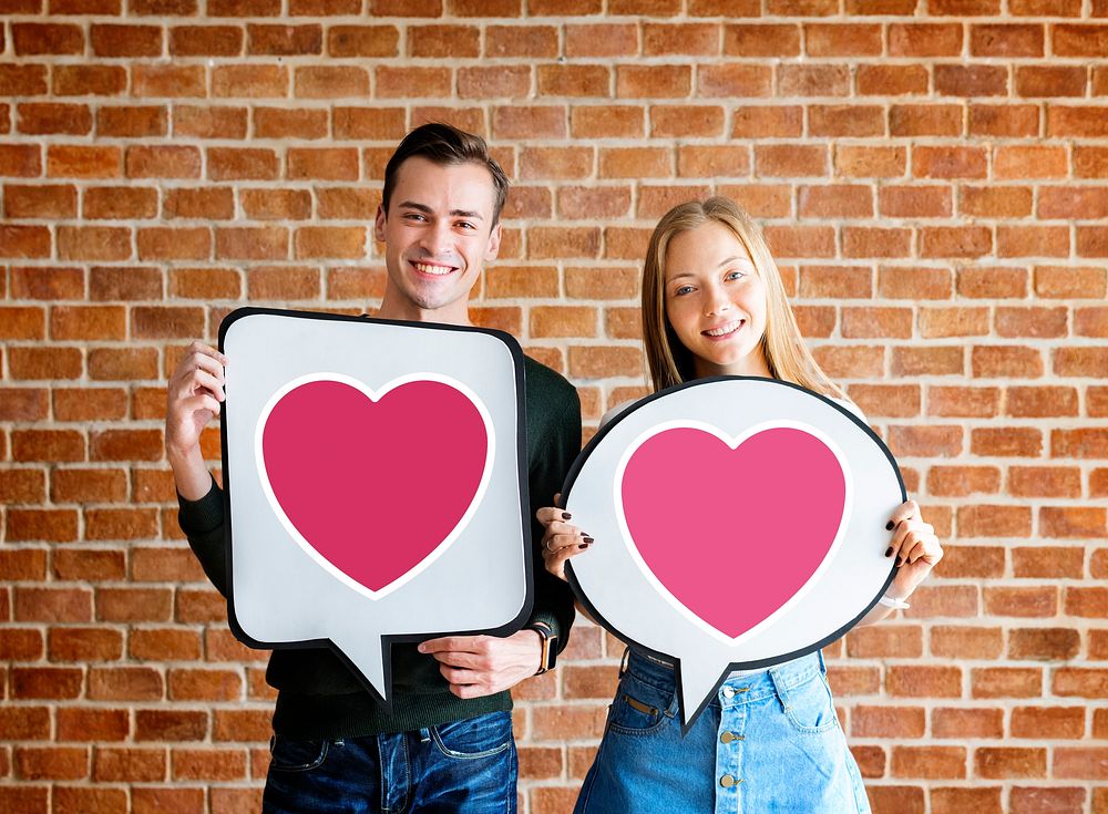 Happy young couple holding speech bubbles with heart icons