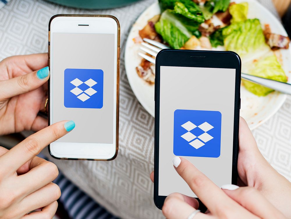 Friends using Dropbox on mobile phones in a restaurant. BANGKOK, THAILAND, 1 NOV 2018.