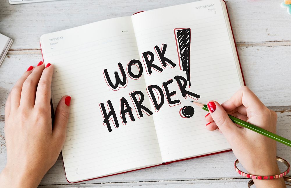 Woman writing Work harder on a notebook