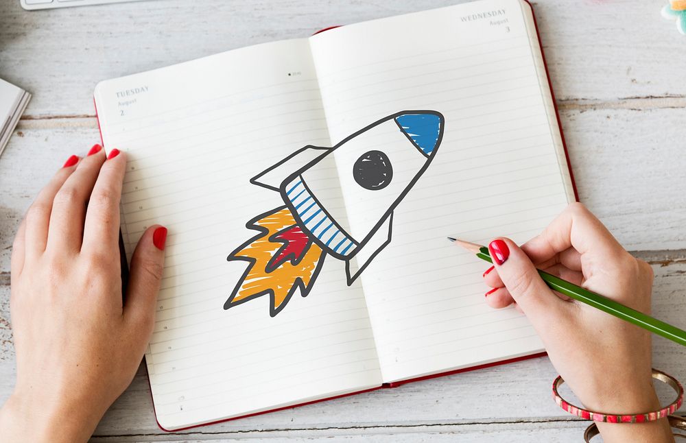 Woman drawing a rocket launch on a notebook