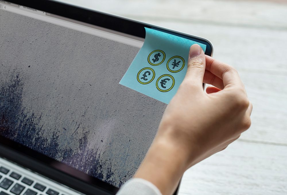 Sticky note with four currencies on a laptop screen