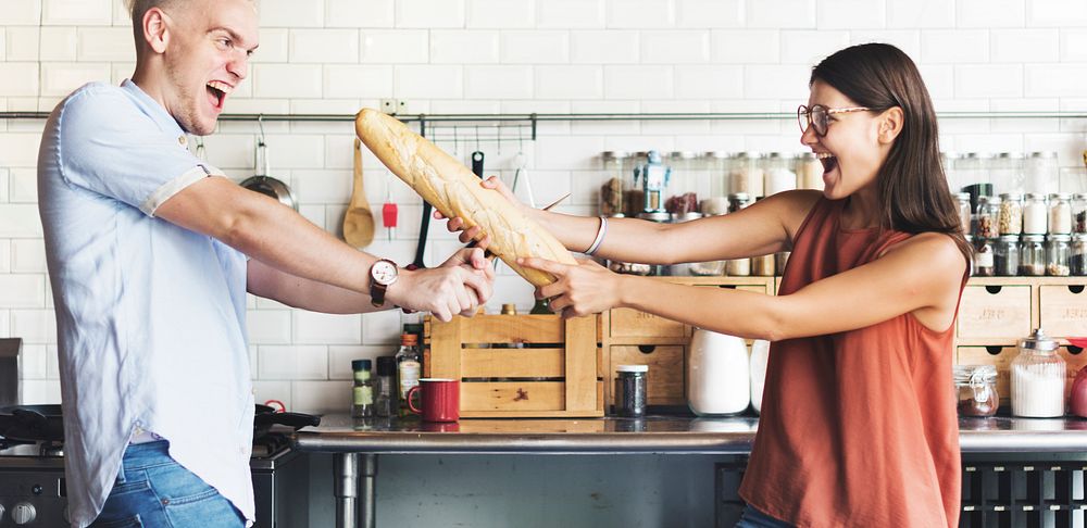 Couple playing together with baguette in kitchen