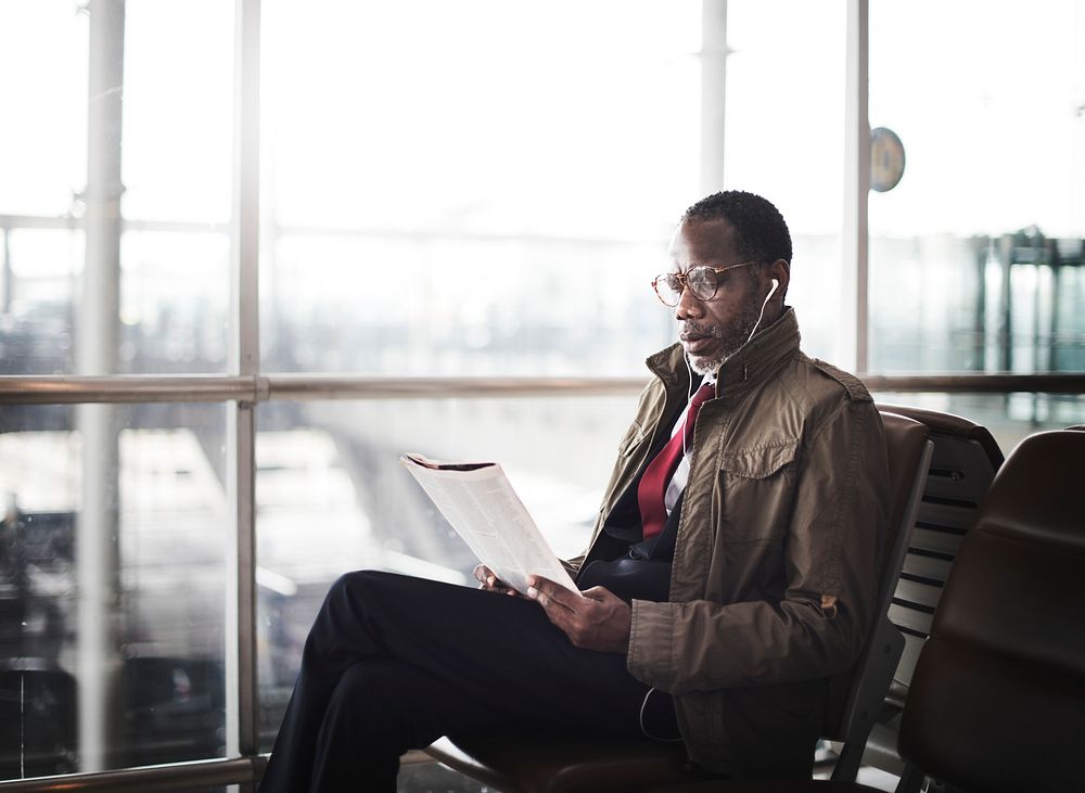 African descent man sitting reading magazine with earphones