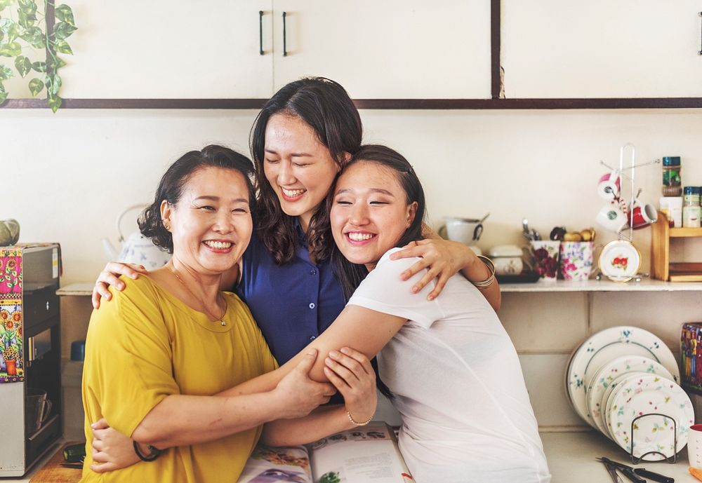 Happy mother and daugthers hugging their mother in a house kitchen