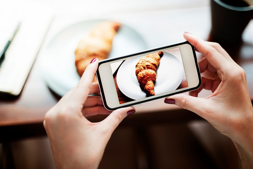 Closeup of hands holding mobile phone taking croissant photo