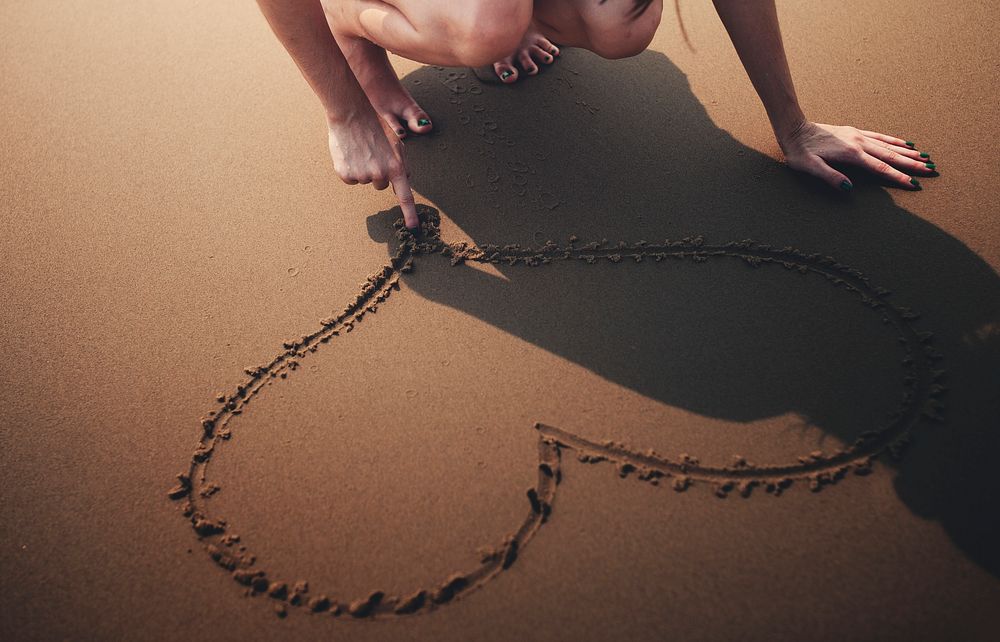 Closeup of hand drawing heart on sand