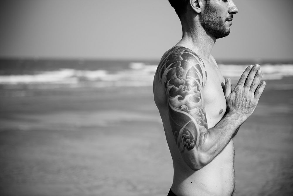 Peaceful man with tattoos meditating by the beach