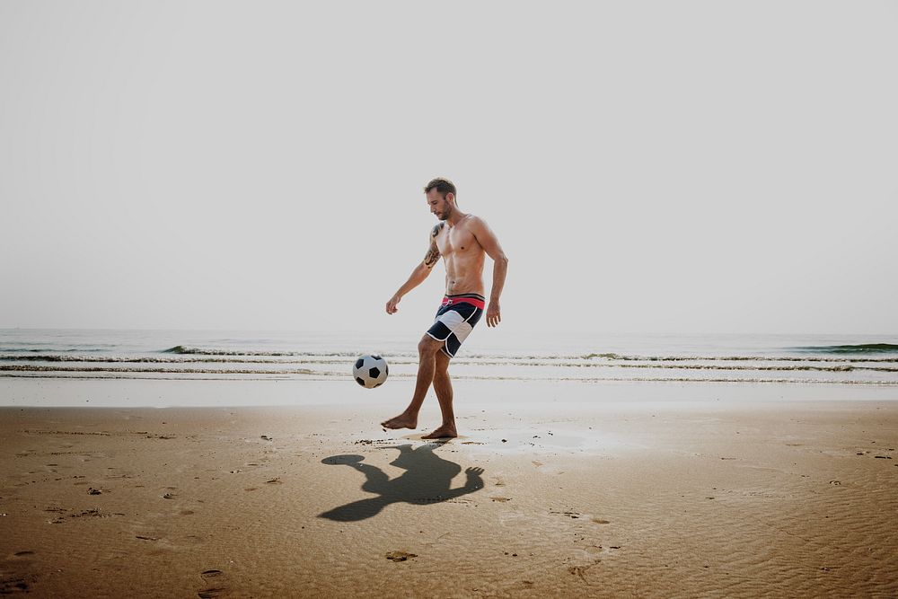 A caucasian man is playing soccer at the beach