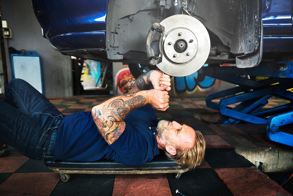 Caucasian auto mechanic man lying reparing car disc brake in garage