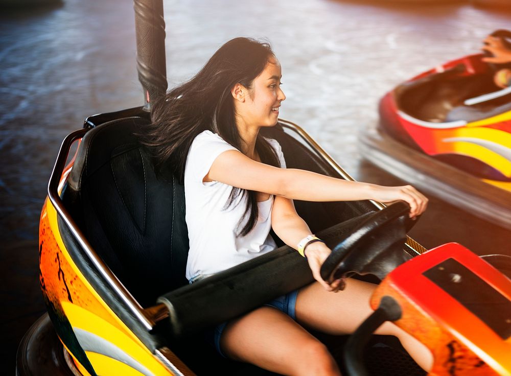 Young adult woman playing in bumper car at amusement park