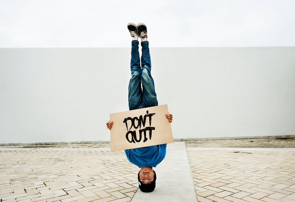 Asian man doing a headstand holding a don't quit banner
