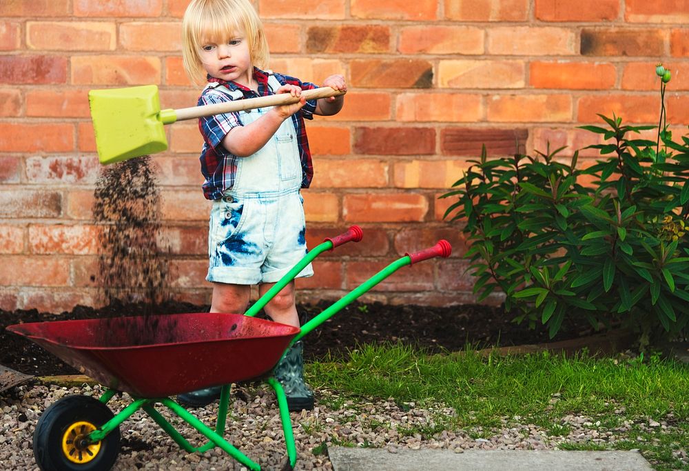 Little boy shoveling soil in a cart