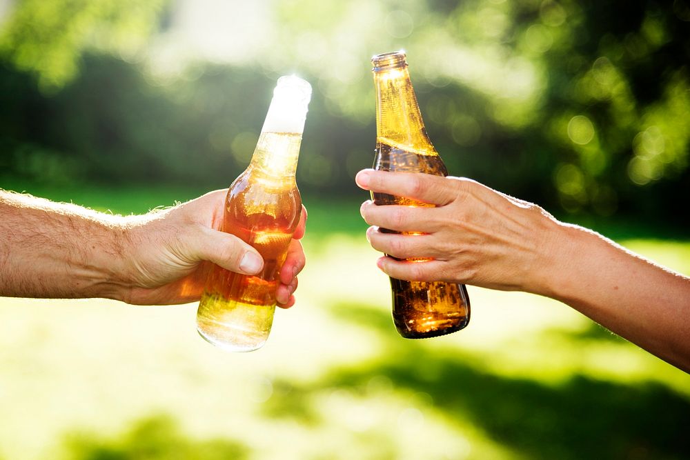 Hands toasting bottles of beer in a park