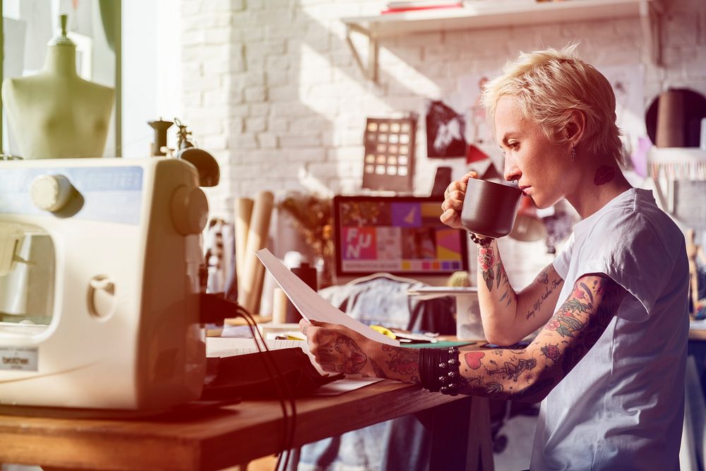 Fashion designer tattooed girl drinking and looking at sketch