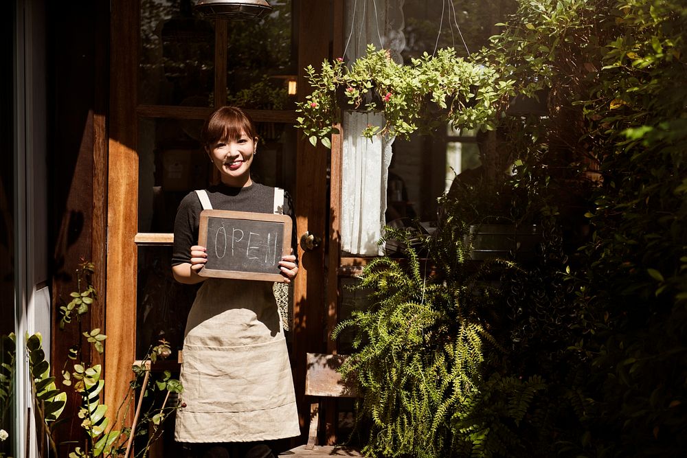 Welcoming woman holding an open sign in front of a cafe shop