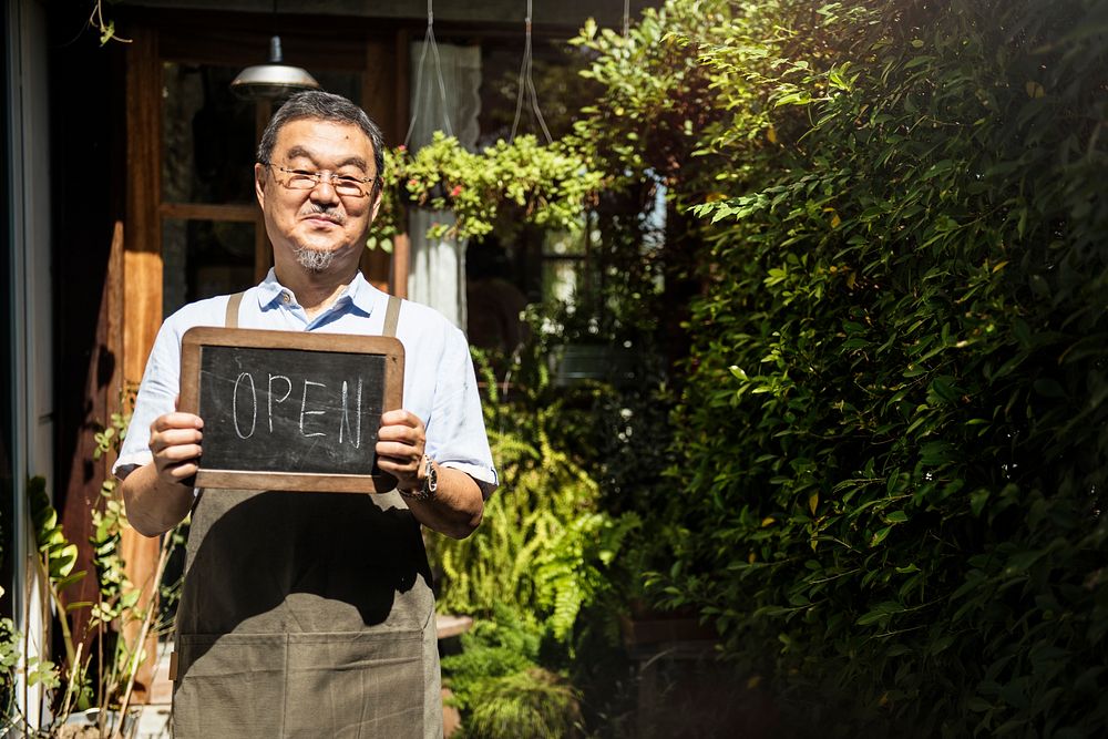 Welcoming senior man holding an open sign in front of a cafe shop