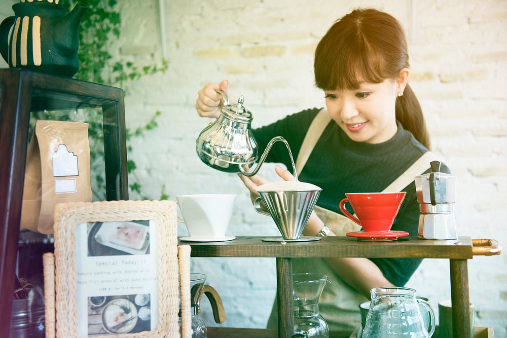 Young woman barista making coffee in cafe