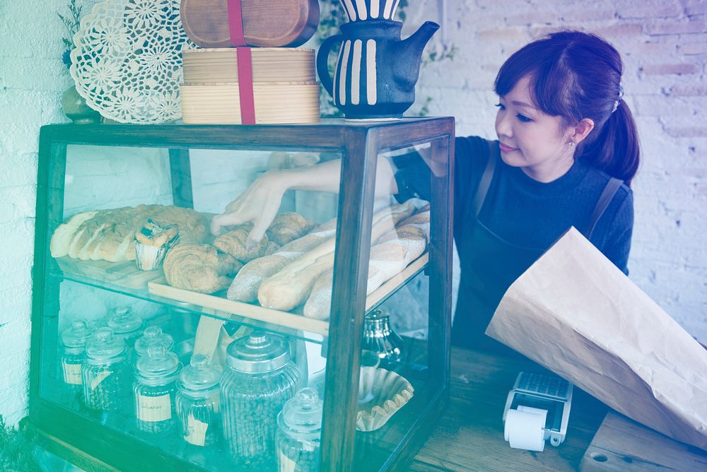 Young patissier woman putting bread pastry on the shelf