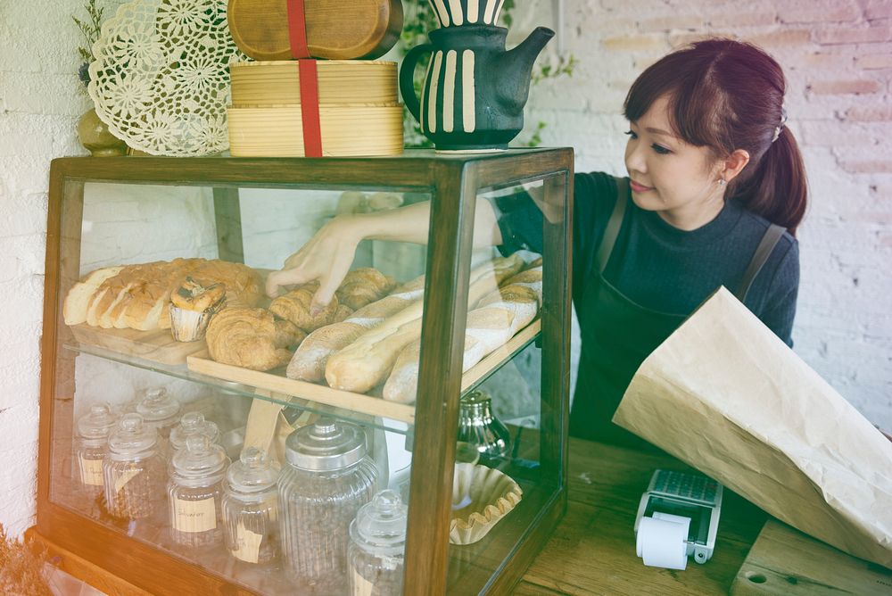 Young patissier woman putting bread pastry on the shelf