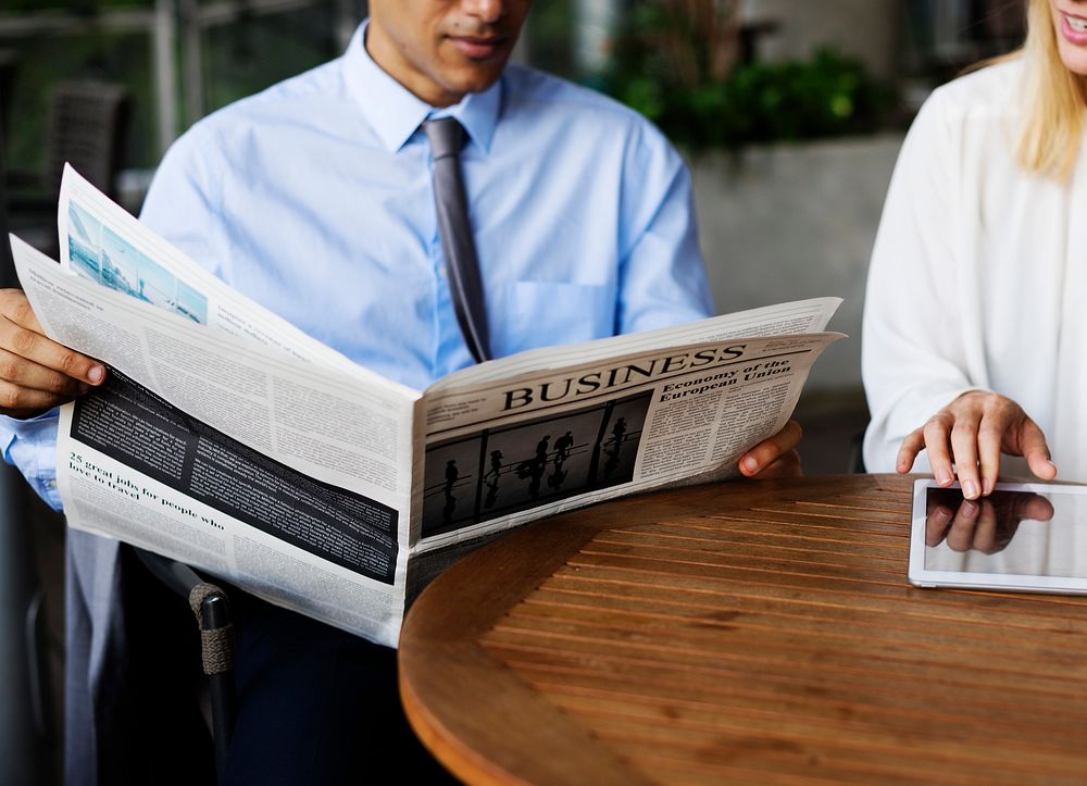 Business man reading newspaper and business woman using a tablet