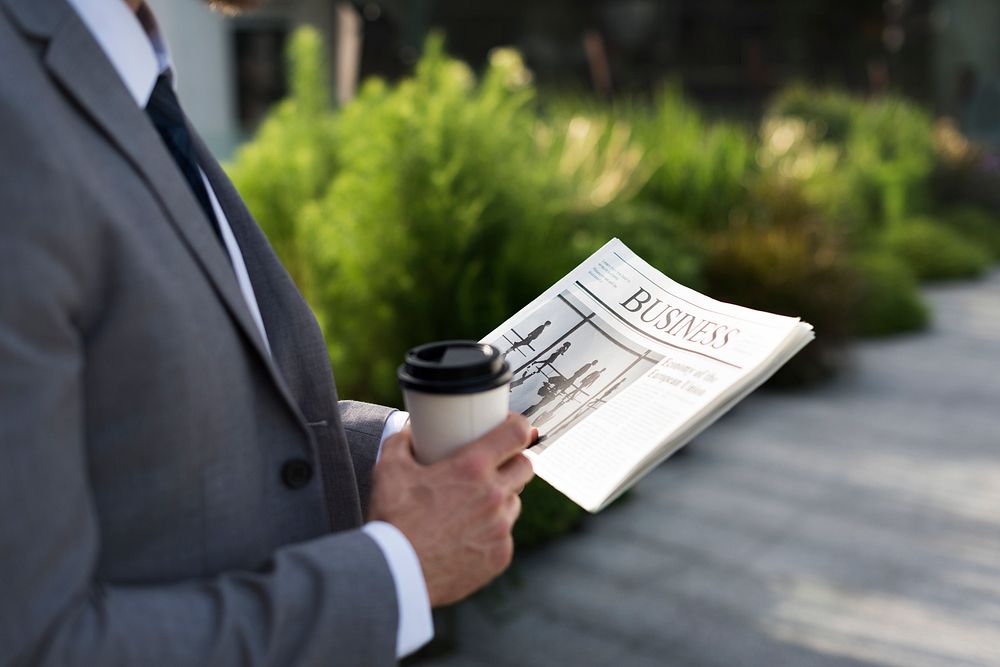 Businessman holding a cup of coffee and reading a newspaper